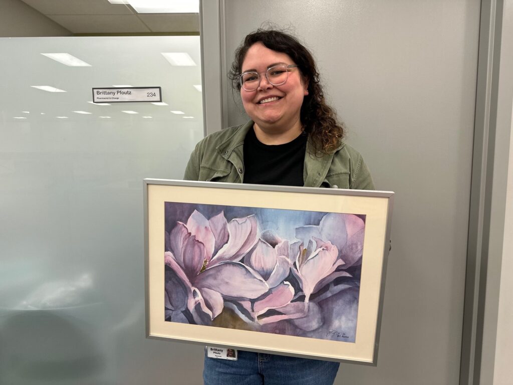 Pfoutz posing with her grandmother’s painting, which she keeps in her office above her desk.