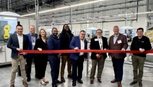 Business leaders cutting red ribbon at warehouse automation facility grand opening ceremony.