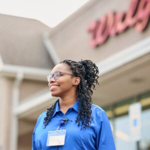 Walgreens employee in blue uniform smiling while looking up outside store entrance.