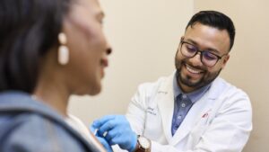Pharmacist in white coat smiling while administering vaccine to patient.