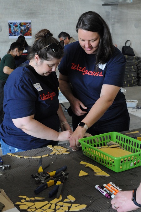 Two females paste mosaic tiles to slab